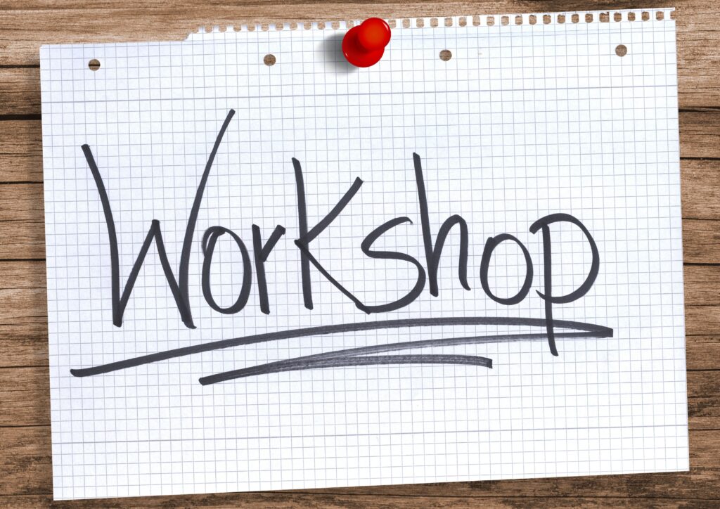 Zettel mit roter Stecknadel an Holz geheftet, Aufschrift „Workshop“.
