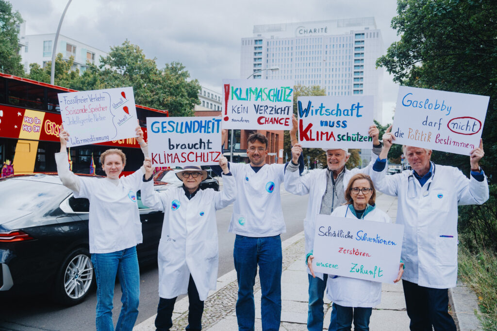 Foto zeigt Gruppe Aktiver in weißen Kitteln und Kasacks, sie halten Schilder mit unterschiedlichen Texten über den Köpfen.